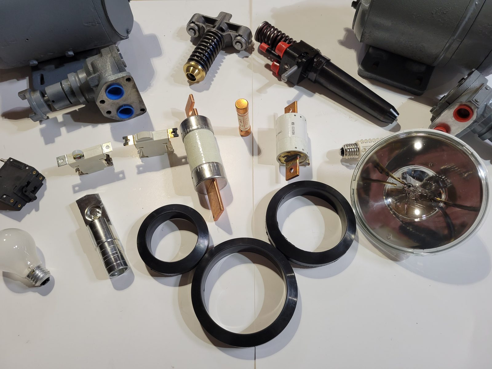 A spread of JMC locomotive parts: fuel injector, valve bridge, fuses, contacts, sealed beam headlight, lamps, seals and blower housings